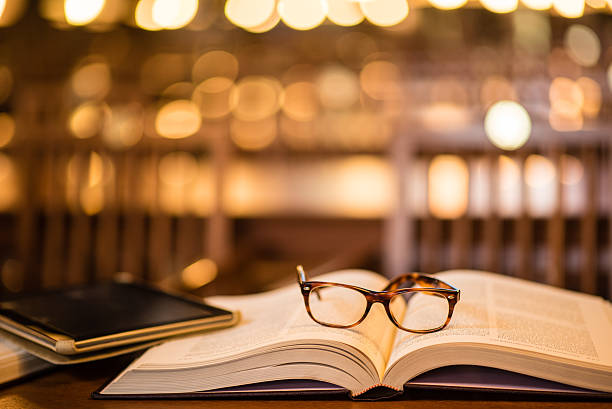 Close-up of reading glasses and digital tablet on book in library.